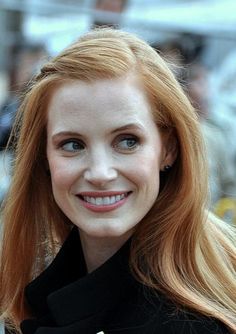 a woman with long red hair smiling at the camera while standing in front of a crowd