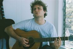 a man sitting down holding a guitar and looking up at the sky with his eyes closed