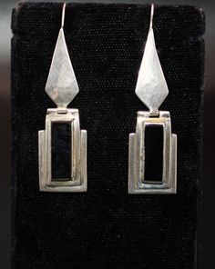 This stunning pair of vintage artisan handmade solid silver and onyx long-drop earrings from the 1980s is a true testament to exquisite craftsmanship. Each earring features a sleek, elongated design with a deep black onyx stone that exudes elegance. The bottom section of the earrings is hinged, allowing for graceful movement that catches the light with every turn. The artisan's attention to detail is evident in the fine silverwork, making these earrings a stylish accessory and wearable piece of Earrings Stones, Graceful Movement, Long Silver Earrings, Black Onyx Stone, Long Drop Earrings, Onyx Stone, Handmade Artisan, Stone Earrings, Stylish Accessories