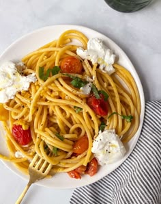 a plate of spaghetti with tomatoes and feta cheese on top, next to a glass of water