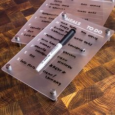 three clear plastic menus with writing on them sitting on a wooden table next to each other