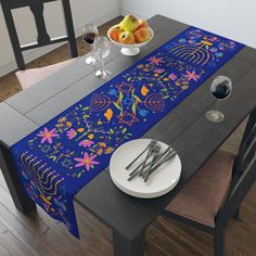 a blue table runner with colorful flowers and fruit on it, along with silverware