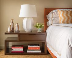 a nightstand with two books on it next to a night stand and lamp in a bedroom