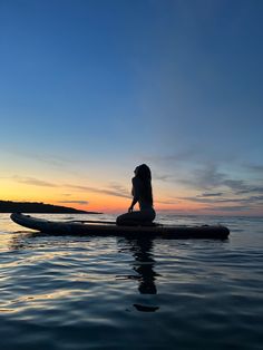 a person is sitting on a surfboard in the water at sunset or dawn,