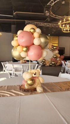 a teddy bear sitting on top of a table with balloons in the air above it