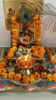 a decorated altar with a lit candle surrounded by flowers and peacock feathers in the background