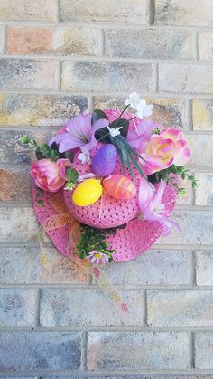 a pink hat with flowers and eggs on it sitting against a brick wall in front of a window