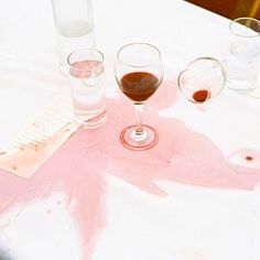 three glasses of wine are sitting on a white tablecloth with pink paint splattered across it