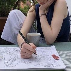 a woman sitting at a table writing on a piece of paper with a cup of coffee in front of her