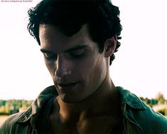 a young man looking down at his cell phone while standing in front of a field