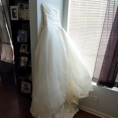 a wedding dress hanging up in front of a window