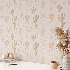 a white table topped with a vase filled with flowers next to a wallpaper covered in cacti