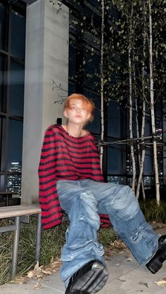 a young man sitting on top of a wooden bench next to a tall building at night