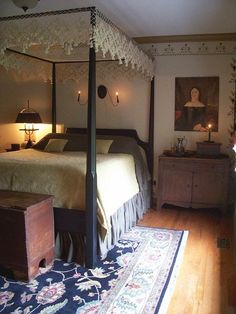 a canopy bed sitting on top of a wooden floor next to a dresser and lamp