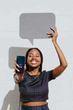 a woman holding up her cell phone in front of a white wall with an empty speech bubble