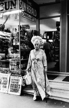 an old woman walking down the sidewalk in front of a sun herald store with her cane