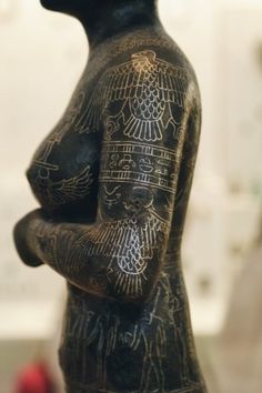 an ancient statue is shown in front of a white wall with writing on the body