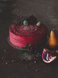 a red cake sitting on top of a table next to a pomegranate