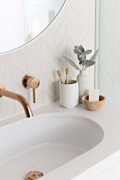 a white bathroom sink sitting under a round mirror next to a potted plant and soap dispenser