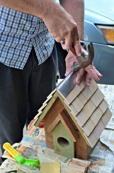 a man holding a wrench over a birdhouse on top of a table covered in papers