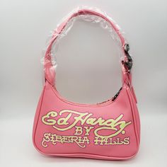 This Ed Hardy X Siberia Hills Y2k Pink Purse Is A Stylish And Trendy Shoulder Bag That's Perfect For Women Who Want To Add Some Pop Of Color To Their Outfit. The Bag Measures 9 Inches In Width And 5 Inches In Height, With A Zip Closure For Security. The Bag's Exterior Is Made From High-Quality Canvas Material And Features A Vibrant Pink Color, While Its Handle And Strap Are Made From Premium Leather Material And Come In A Matching Pink Shade. The Bag's Interior Lining Also Comes In Pink And Has Ed Hardy Bag, Pink Y2k Shoulder Bag For School, Pink Rectangular Y2k Bag, 2000s Purse, Y2k Things, Y2k Pink Shoulder Bag, Ed Hardy Purse, Siberia Hills, Pink Hello Kitty Print Shoulder Bag