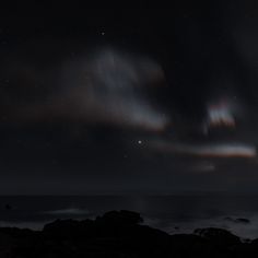 the night sky is filled with stars and clouds over the ocean as seen from rocky shore