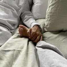 a man laying on top of a bed covered in white sheets and pillows with his hands resting on the pillow