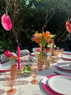 the table is set with pink and orange flowers in vases, plates, and candles