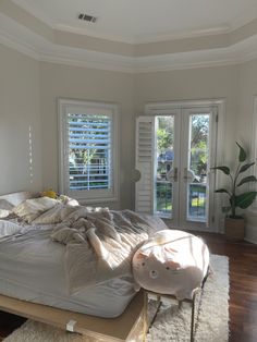 an unmade bed sitting on top of a wooden floor next to two large windows