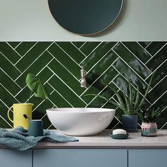 a bathroom with green tiled walls and white counter tops, blue cabinets and a round mirror on the wall