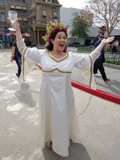 a woman in a white dress is holding her arms out with both hands as she stands on the sidewalk