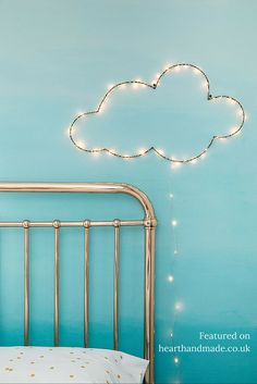 a bed with a gold headboard and a cloud shaped string light above it on the wall