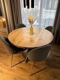 a round wooden table with four chairs around it and a vase on top of the table