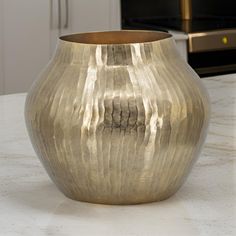 a large metal vase sitting on top of a white counter next to a oven and microwave