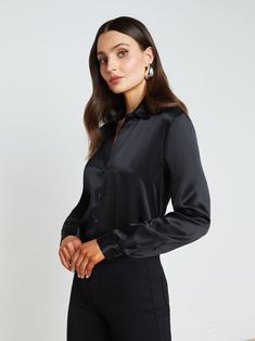 A quintessential blouse in a lustrous silk charmeuse and true black hue. Classic look has a soft, liquid hand and tailored silhouette shaped by sharp sartorial details like a stand collar, long button-cuff sleeves, and back yoke with inverted pleat. An open neckline and curved hem add subtle femininity. A nimble style that works equally well with jeans or skirts. Fastens in front with tonal buttons. | L'AGENCE Tyler Silk Blouse Top In Black Elegant Silk Top For Business, Chic Silk Business Blouse, Chic Silk Blouse For Business, Elegant Semi-formal Blouse With Button Closure, Timeless Formal Blouse With Button Closure, Classic Silk Blouse For Formal Occasion, Elegant Tops With Button Closure, Sleek Satin Button-up Blouse, Sleek Silk Tops For Business