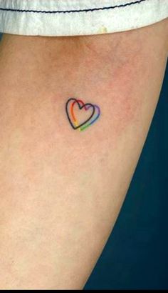 a small heart tattoo on the back of a woman's leg, with an orange and blue stripe in the shape of a rainbow