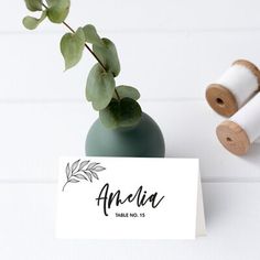 a table number card with a plant in a vase next to two spools of twine