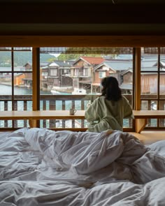 a woman sitting on top of a bed in front of a window with lots of white sheets