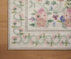 a white rug with pink flowers and green leaves on the bottom is laying on a wooden floor