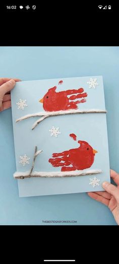 someone is holding up a handprinted cardinal on a branch with snowflakes