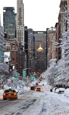 a city street covered in snow and surrounded by tall buildings with cars driving down it