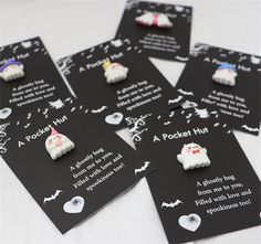 four black tags with white and pink ghost buttons on them, one says pocket hug