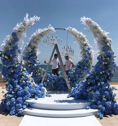 two men standing in front of an arch decorated with blue and white flowers