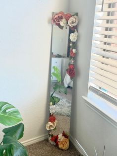 there is a mirror with flowers on it next to a potted plant in the corner