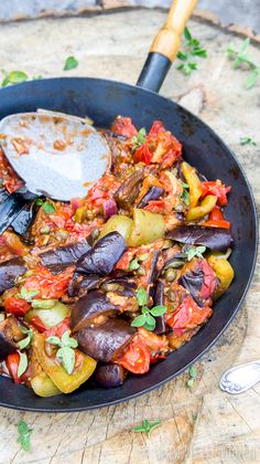 a skillet filled with cooked vegetables on top of a wooden table next to a spatula