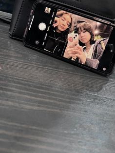 a cell phone sitting on top of a wooden table next to a black case with two women's faces