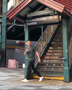 a man standing in front of a train station next to a set of stairs with a sign that reads knickkerboker av station