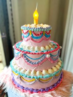 a three tiered cake with a lit candle on it's top and pink feathers around the edges