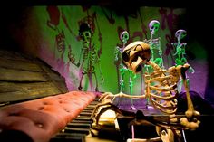 a skeleton sitting on top of a piano next to an orange bench and green wall