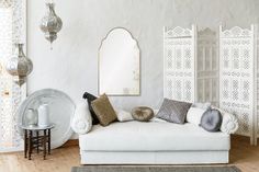 a living room with white furniture and decorative mirrors on the wall, along with rugs